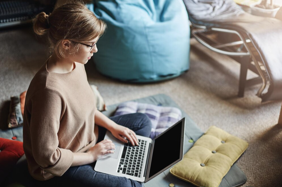 woman in the cozy outfit and glasses sitting on the floor with a laptop on lap