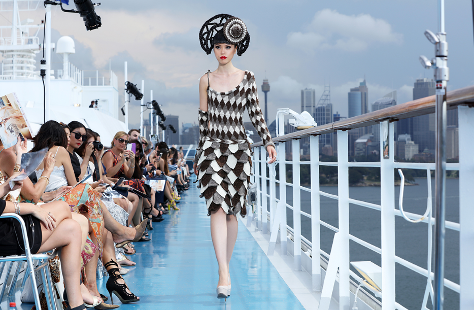 a woman in a "geometric" dress and hat defiling during the fashion event on a ship