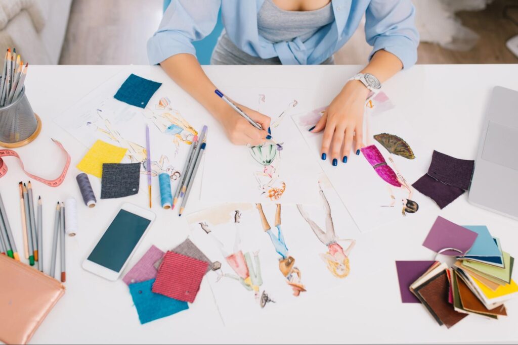 a woman with blue nails sitting at the table designing clothes and drawing sketches