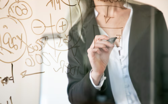 woman in suite writing on glass board with pen