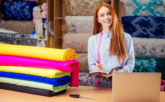 A girl standing in a fabric store, holding a pen and notebook while surrounded by various fabrics