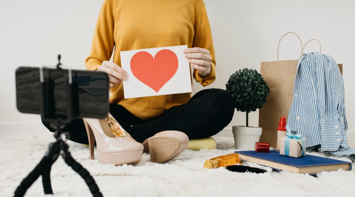 woman holds a sheet with a heart on it and records a video, flowers, book on the fluffy white carpet