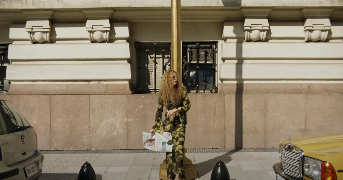 Girl on a city street post, wearing sunglasses, holding a newspaper