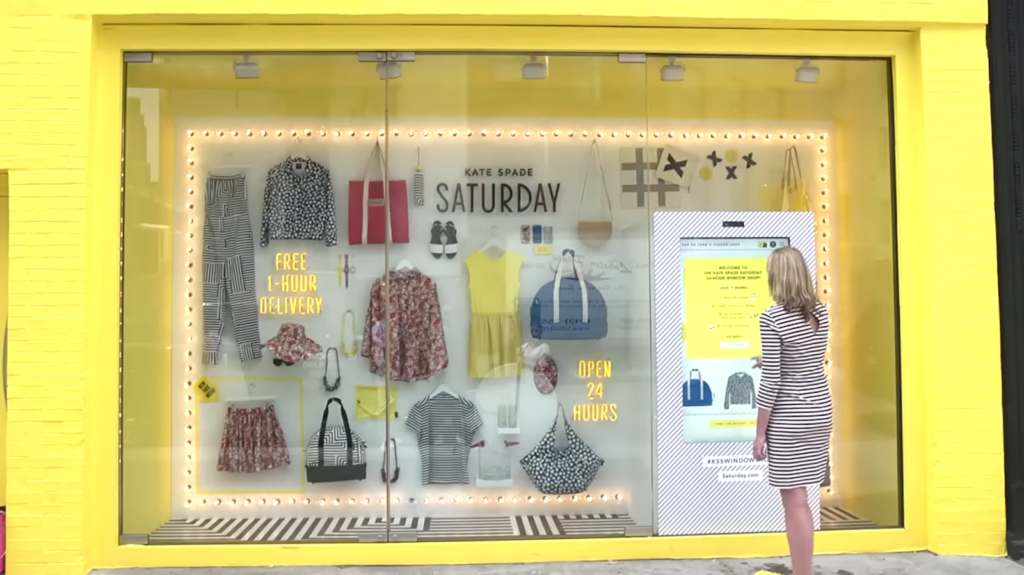 a woman standing near the yellow shop with clothes and bags on in the windows