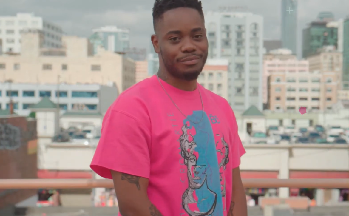 man in pink t-shirt standing among the city and smiling