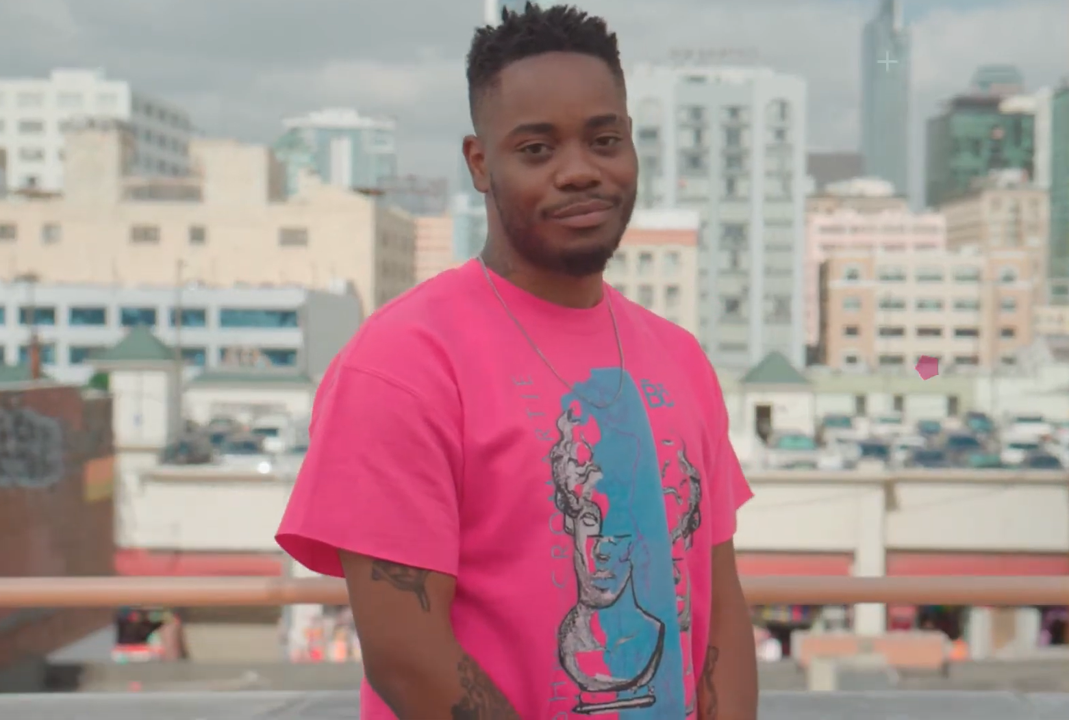 man in pink t-shirt standing among the city and smiling